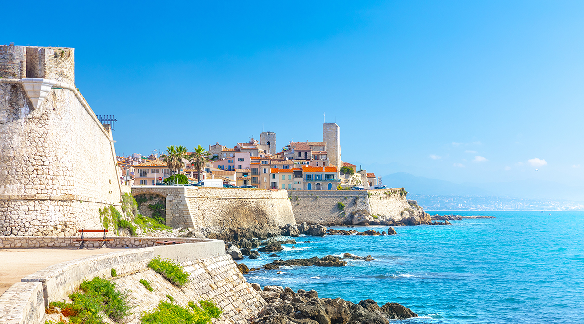 Picturesque town filled with white brick buildings with orange tiled roofs in the distance on a bay filled with blue waters and a blue sky